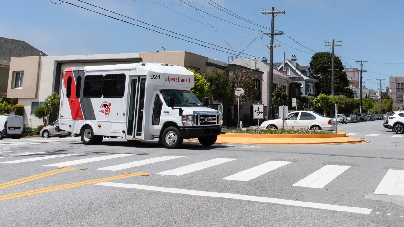 A paratransit van drives through an intersection with a traffic circle.
